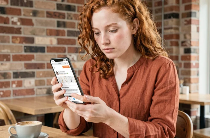 Jeune femme consultant les avis clients et les indicateurs de sécurité d'une boutique de bijoux en ligne sur son smartphone dans un café